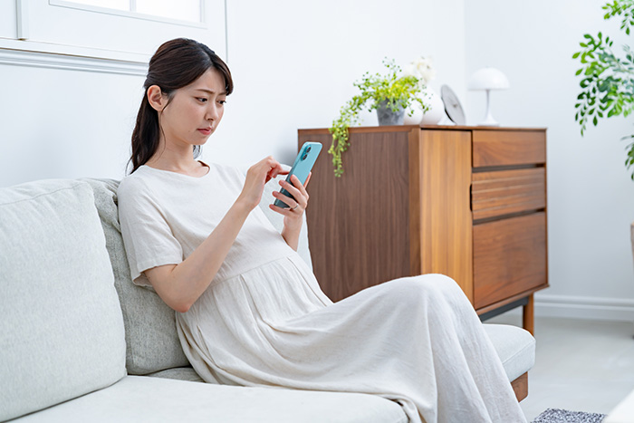 妊娠中に歯が痛くなって歯科医院に電話をかけるかどうかスマホを手に悩む女性