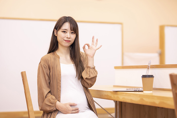 妊娠中の女性が手でOKサインを笑顔で作っている画像